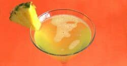 Overhead view of Cabo drink with pineapple wedge against orange background