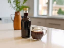 Bottle of homemade Kahlua liqueur next to a cup of coffee