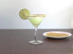 Pale green Key Lime Martini in glass with lime wheel and graham cracker crumb rim