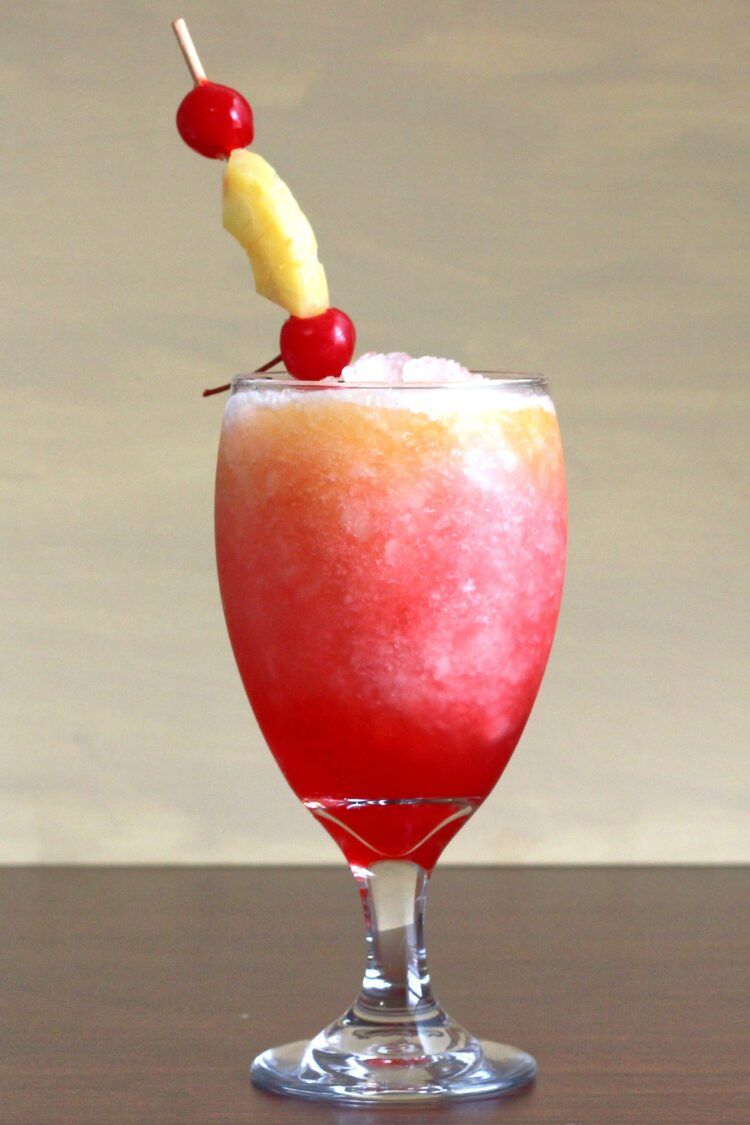 Red and orange Kiss on the Lips drink with pineapple and cherry garnish