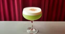 Green Matcha Pisco drink in coupe glass with white foam on top
