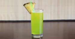 Bright green Monkey In a Tree drink with pineapple wedge garnish on table