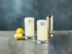 Two Silver Fizz drinks in tall glasses beside cut lemons