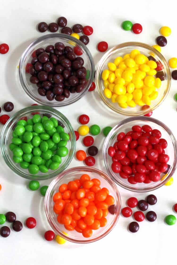 Skittles separated into bowls by flavor and scattered on table
