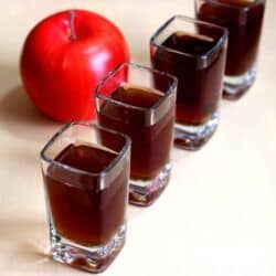 Four Sour Apple Pie shooters lined up beside apple