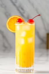 Yellow Bird drink with orange and cherry garnish